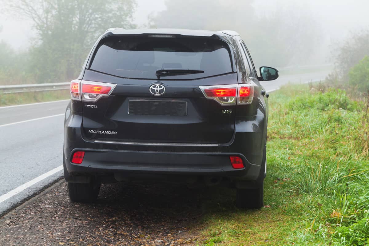 Black Toyota Highlander car stands on a roadside in foggy morning