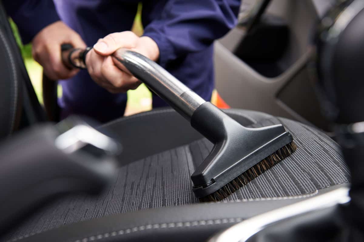 Car technician cleaning the driver seat using a vacuum