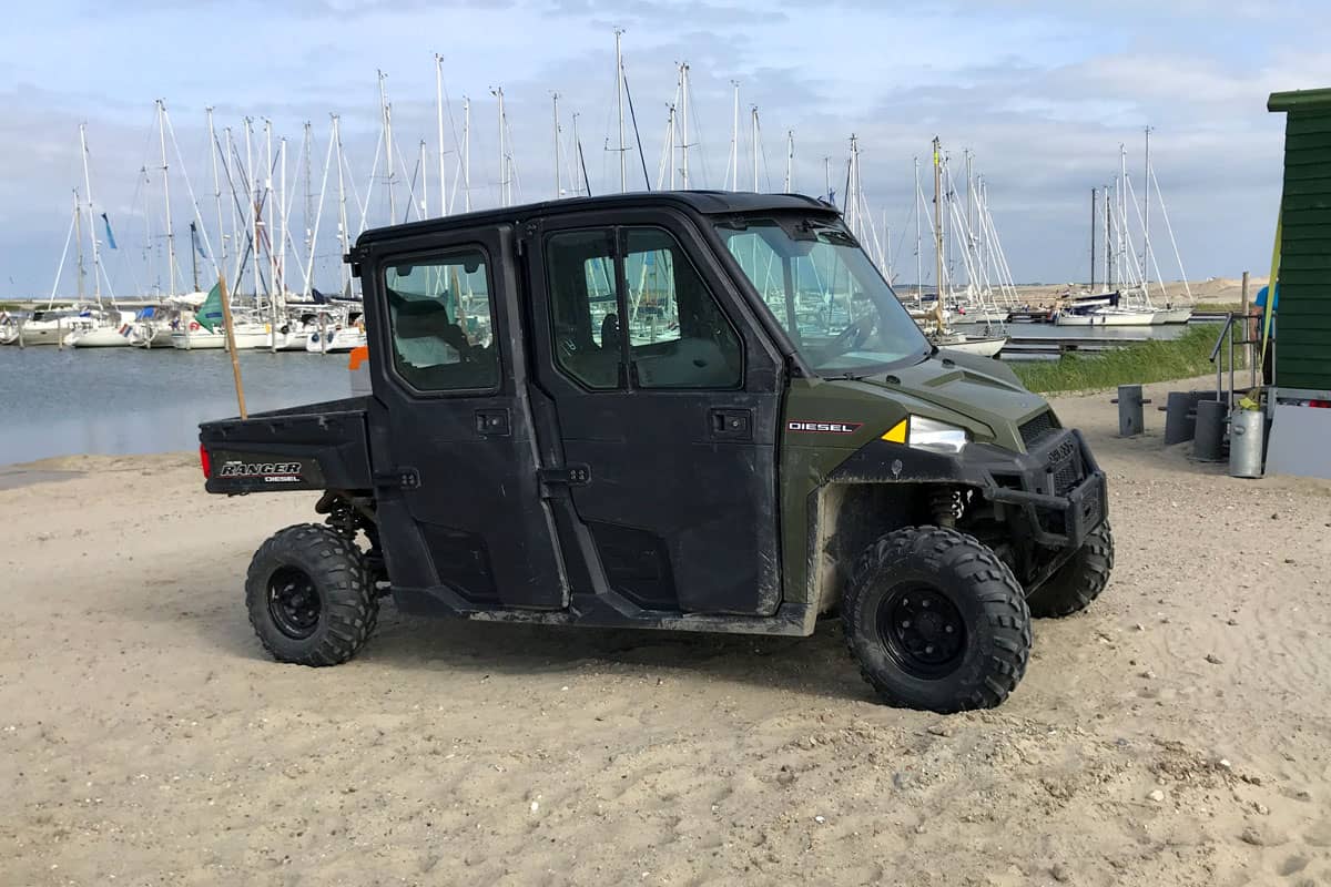 Green Polaris Ranger Crew parked on a beach. Nobody in the vehicle