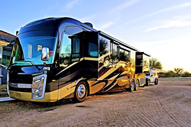 Luxury Motorhome recreational vehicle RV parked on dirt lot at sunset with reflections of trees