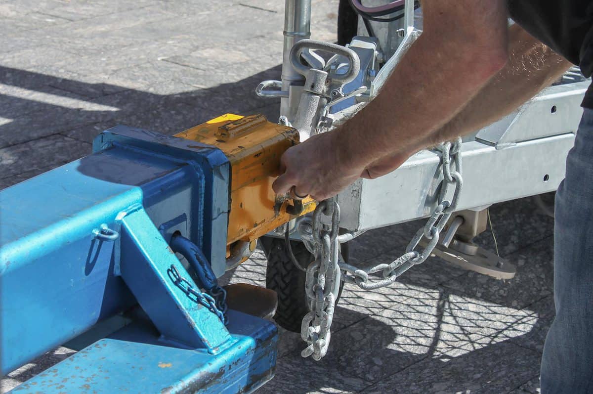 Man fastening a chain onto an industrial hitch on a trailer