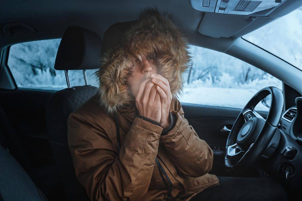 Man in down jacket tries to keep warm and not freeze in his stalled car in winter