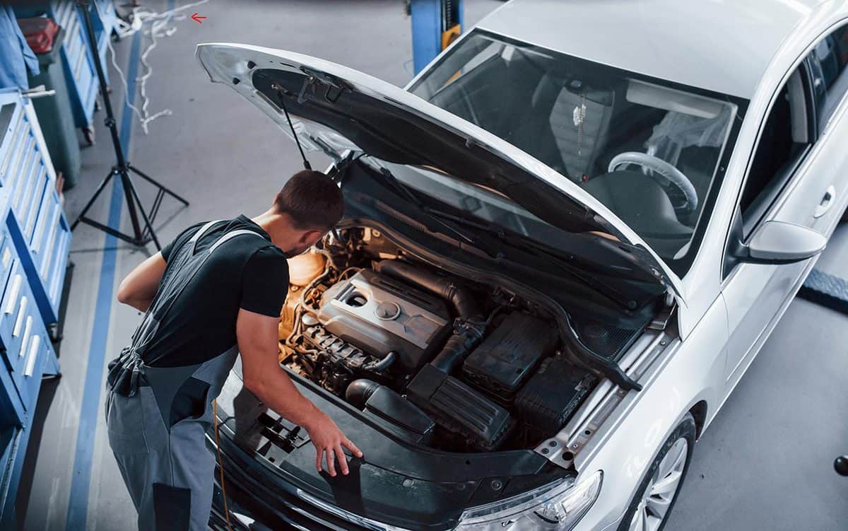 Man in grey uniform repairs white automobile indoors