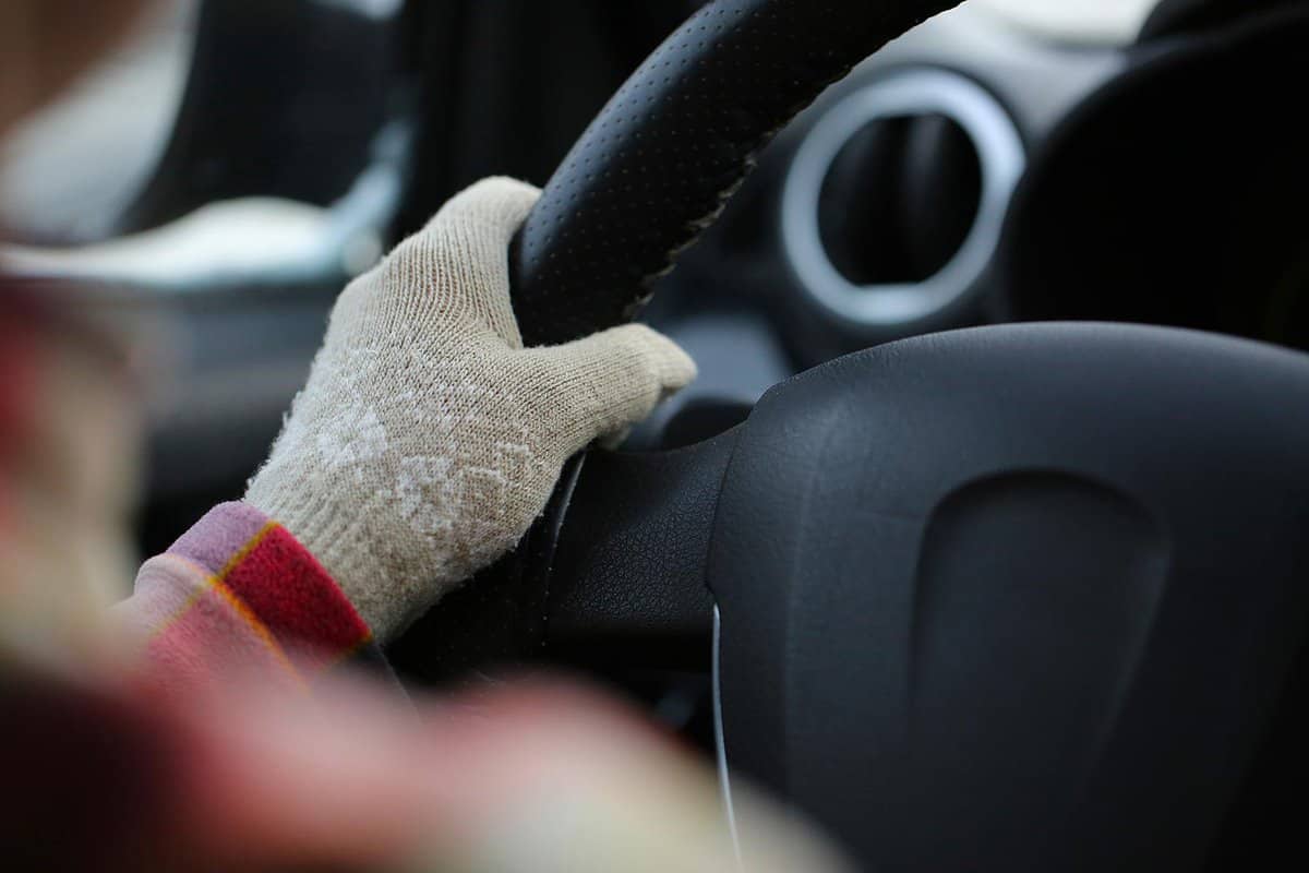 One hand in female beige glove on steering wheel