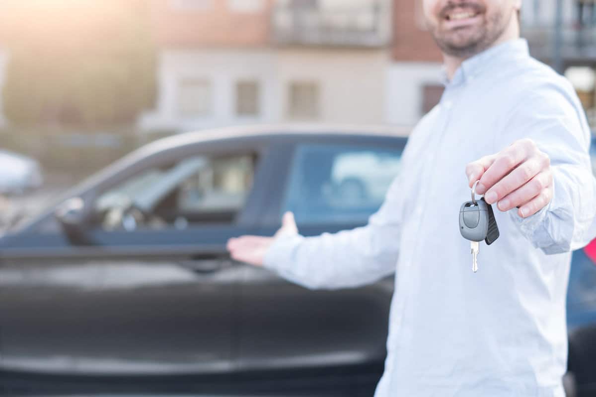 One man holding a car key next to his vehicle , main focus on the hand