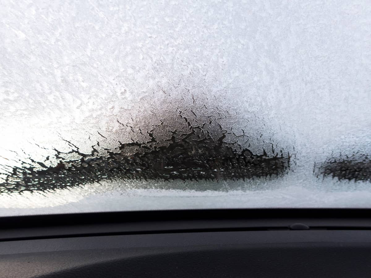Part of a car's windshield covered with ice. Looking across the dash at the defrosting ice.