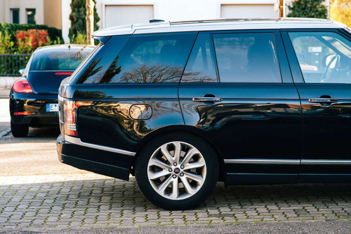 Side view of Land Rover Range Rover luxury SUV car parked on a french street with VW Beetle