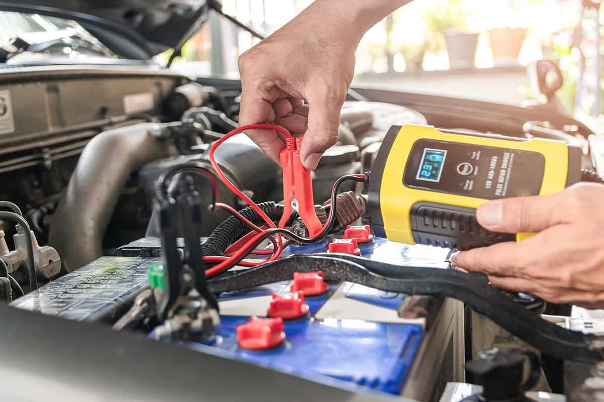 The car mechanic is using a voltage measuring instrument and charging the battery