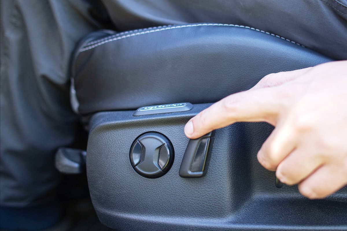 The man presses his finger on the adjustment button for the electric seat in the car. Modern comfortable seat