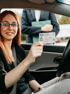 Young woman successfully passed a driving test at a driving school. She is holding a driving license - Can You Drive With A Picture Of Your License Is This Illegal