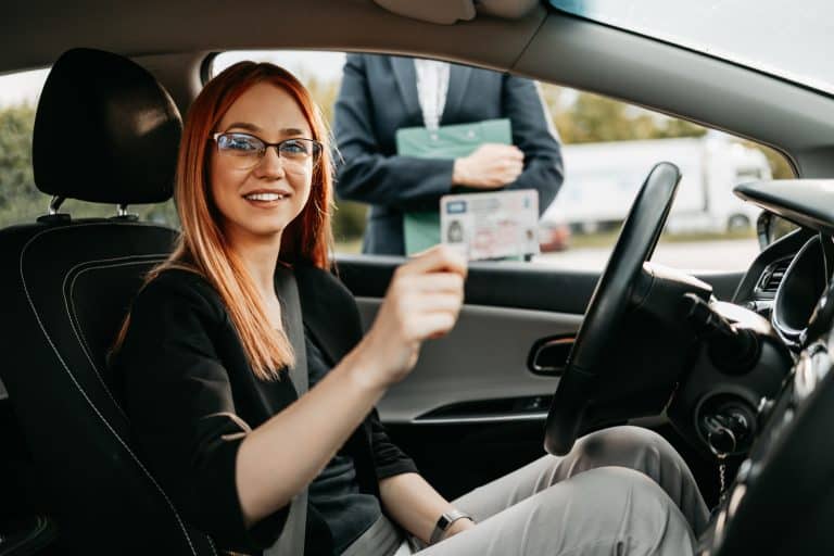 Young woman successfully passed a driving test at a driving school. She is holding a driving license - Can You Drive With A Picture Of Your License Is This Illegal