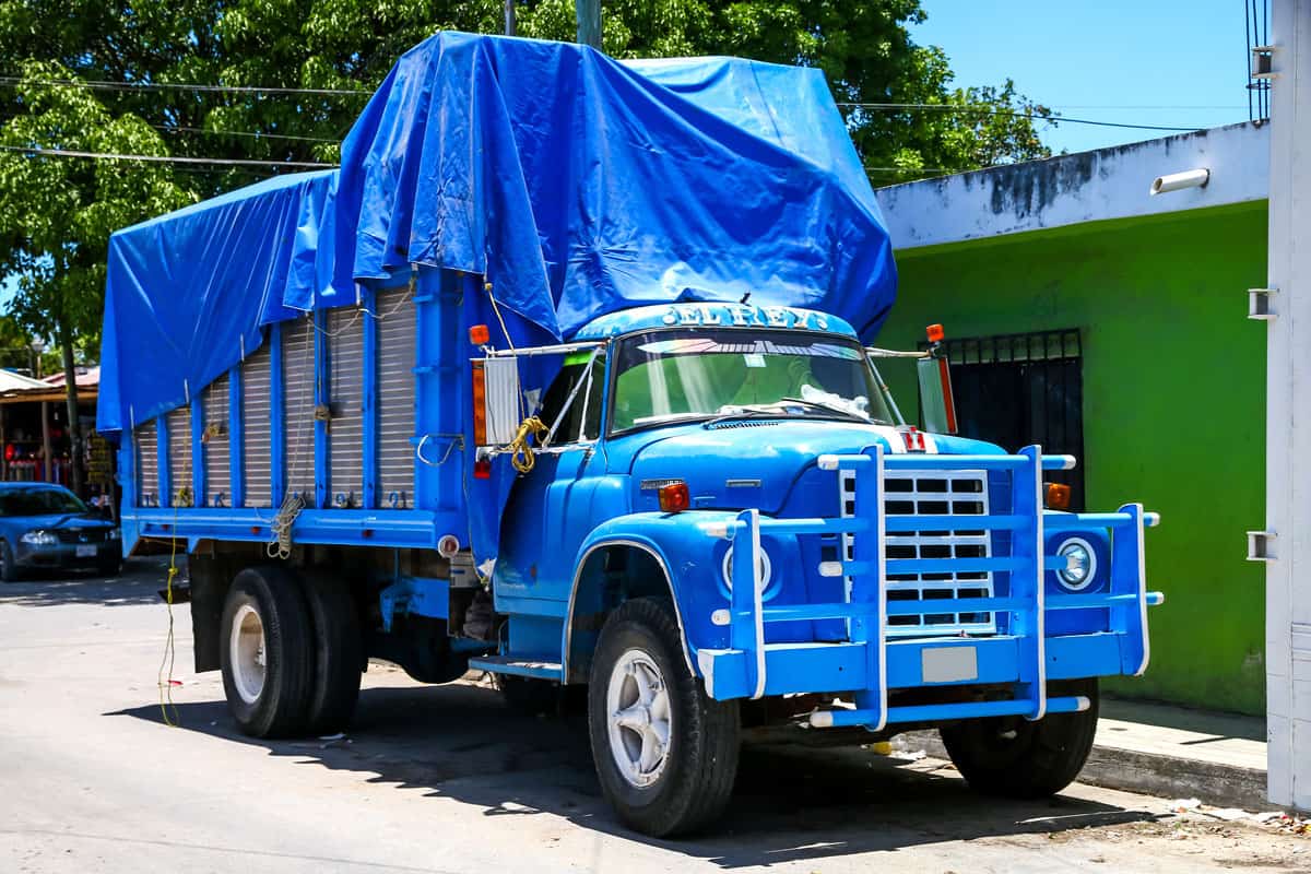 A huge black truck with blue painted bull bar and covered with blue tarp