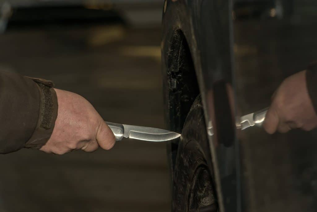 A man holds a knife in his hand and wants to sting with it in a car tire. 
