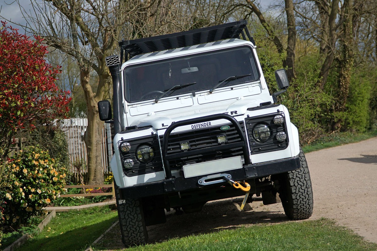 A white Land Rover Defender with a black bull bar with fog lights installed on it