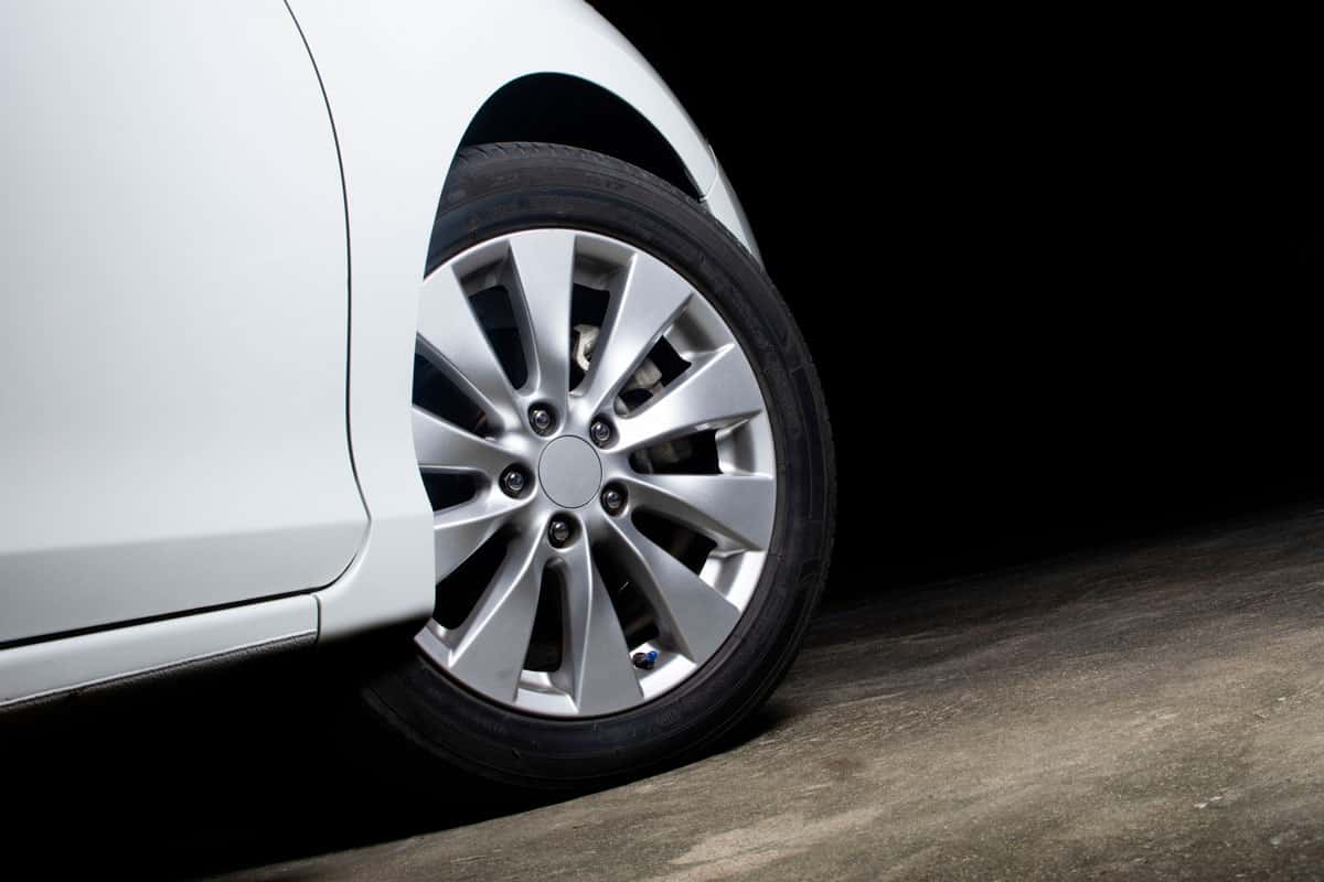 Alloy wheels of a white car are turning on the cement road of parking lot