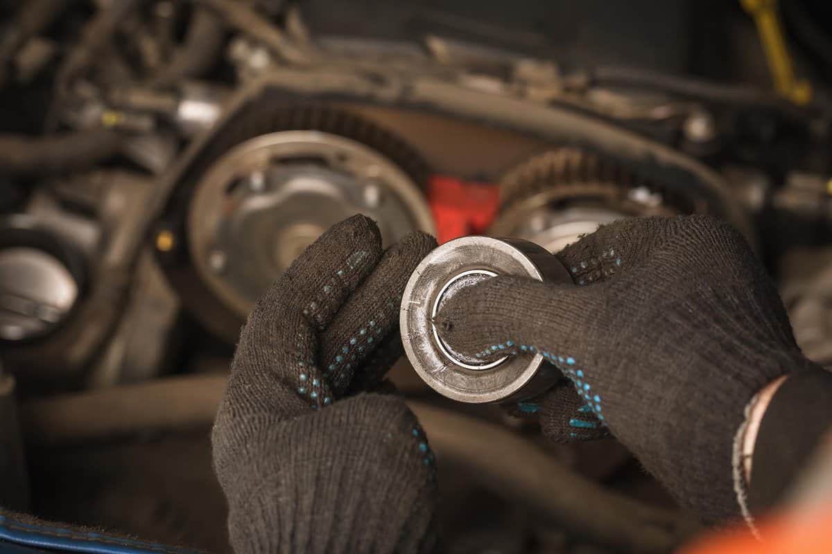 An auto mechanic checks the condition of the timing belt tensioner roller of a passenger car