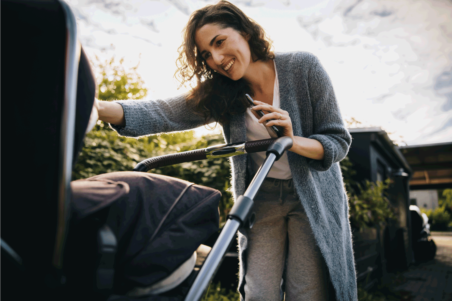 Cheerful mother pushing a stroller and looking at her baby. Happy mother with stroller outdoors.