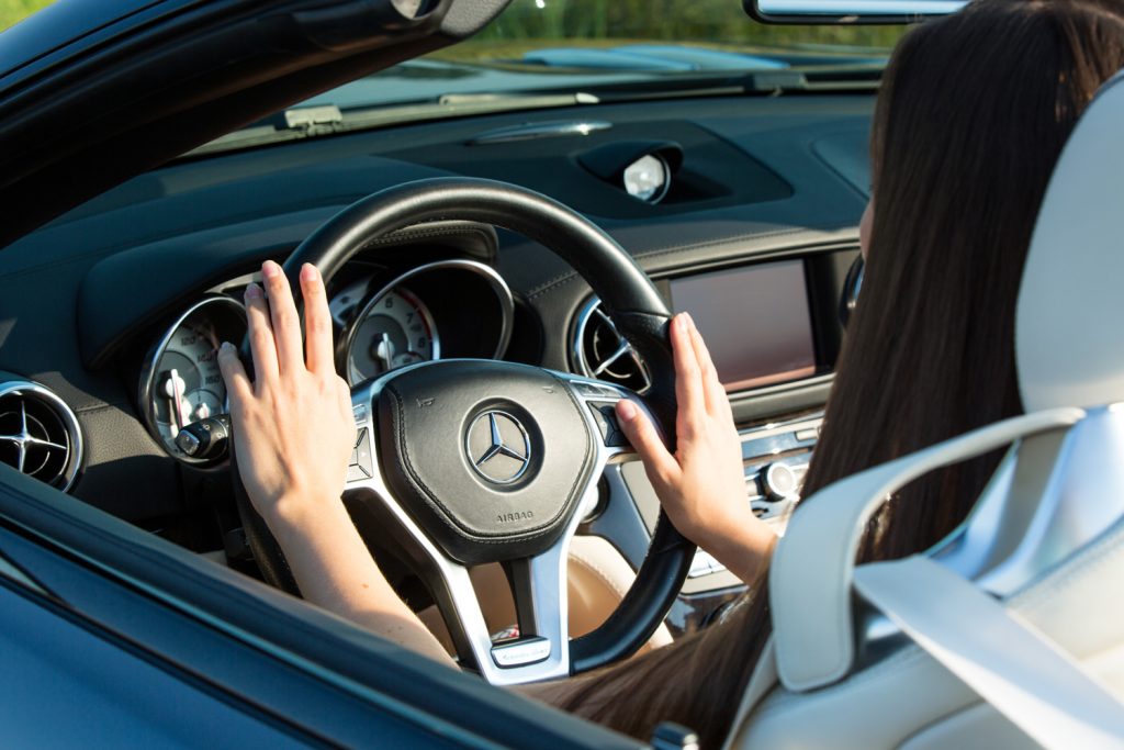 Closeup on female hands driving Mercedes Benz car luxury transportation lifestyle. Mercedes Benz SL550 convertible on the road