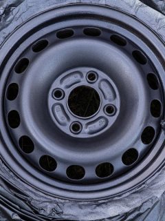 Diy maintenance at home fixing up an old weathered car tire by spray painting new fresh metallic top paint on the wheel cap while covering the black rubber with plastic to keep it clean and protected.
