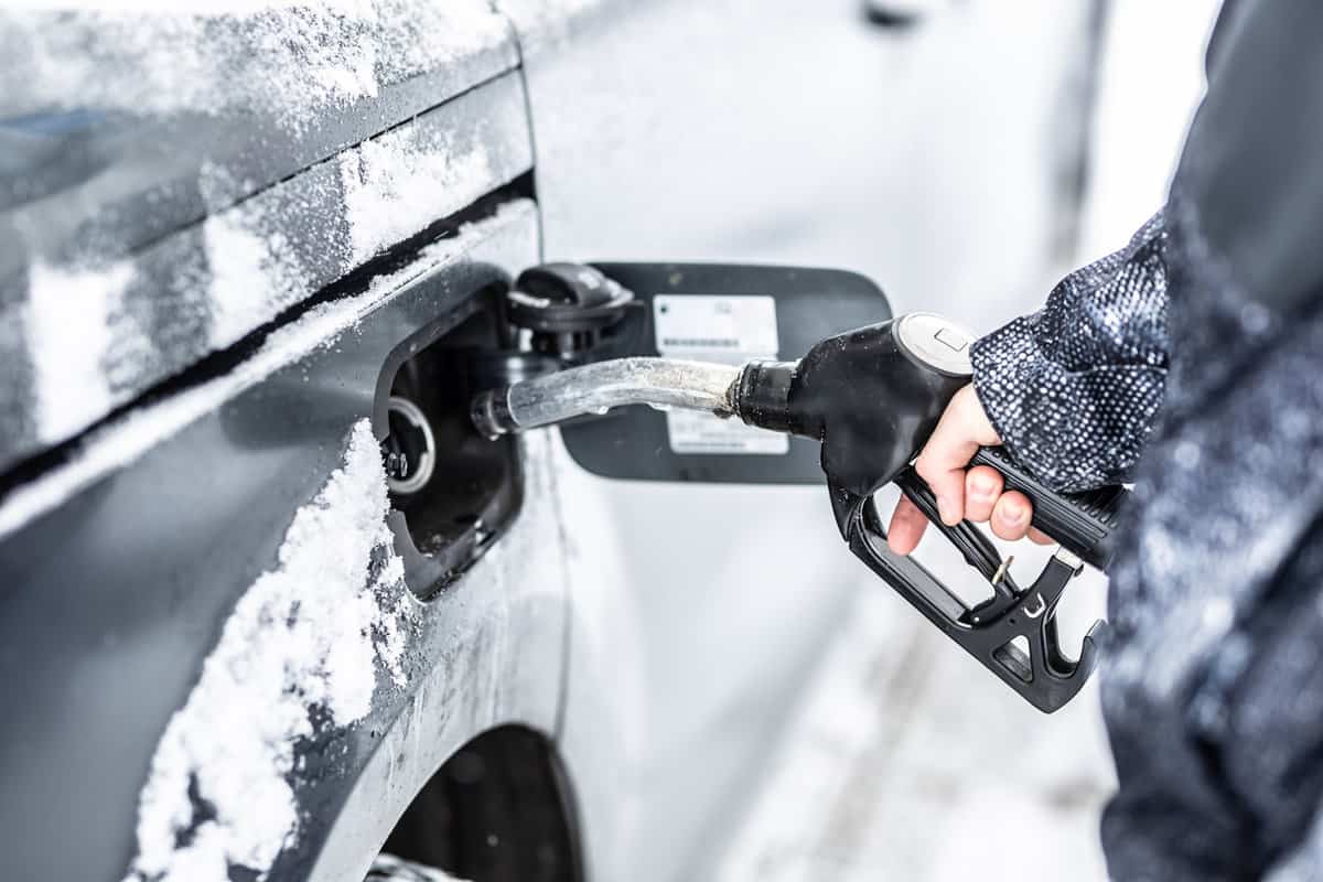 Hand of a man filling up the fuel tank of his car during freezing snowy winter.