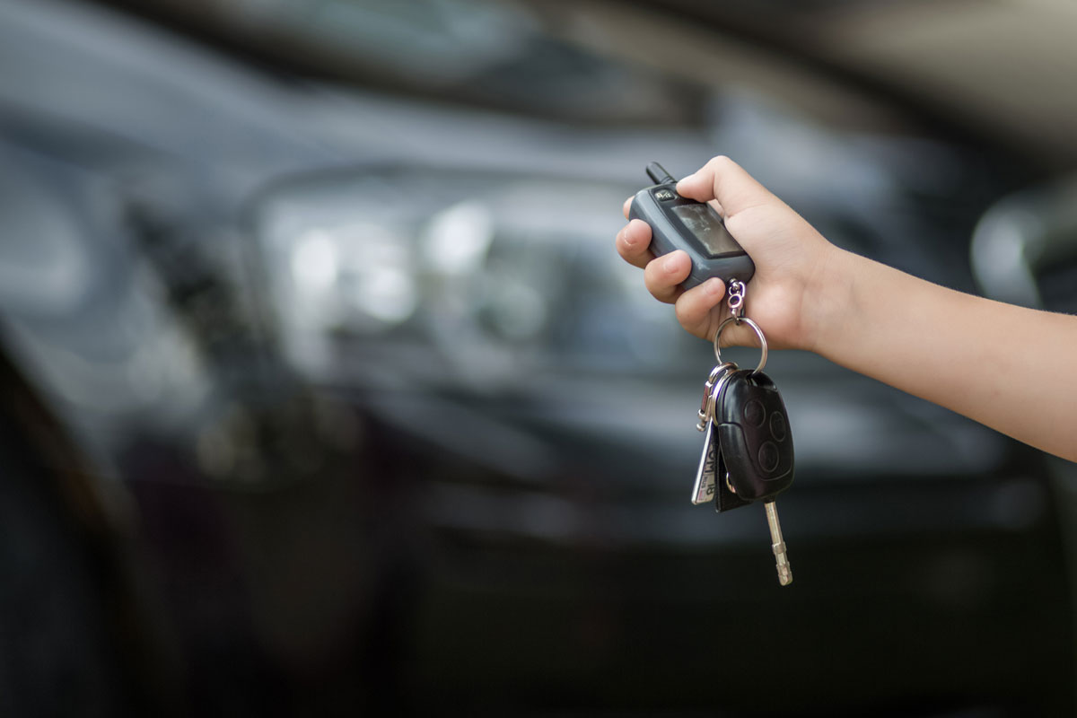 Hand of the child holds the car keys and a blurry background of a black car