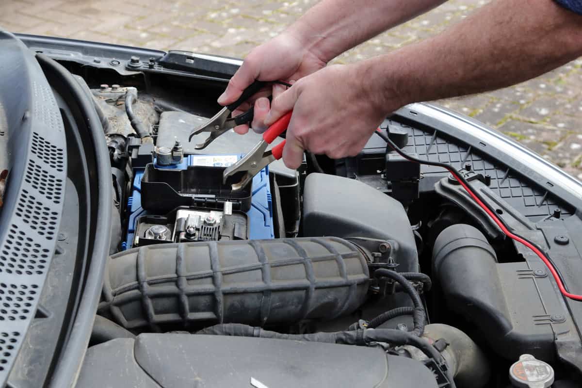 Hands with cables charging up a car battery in engine bay