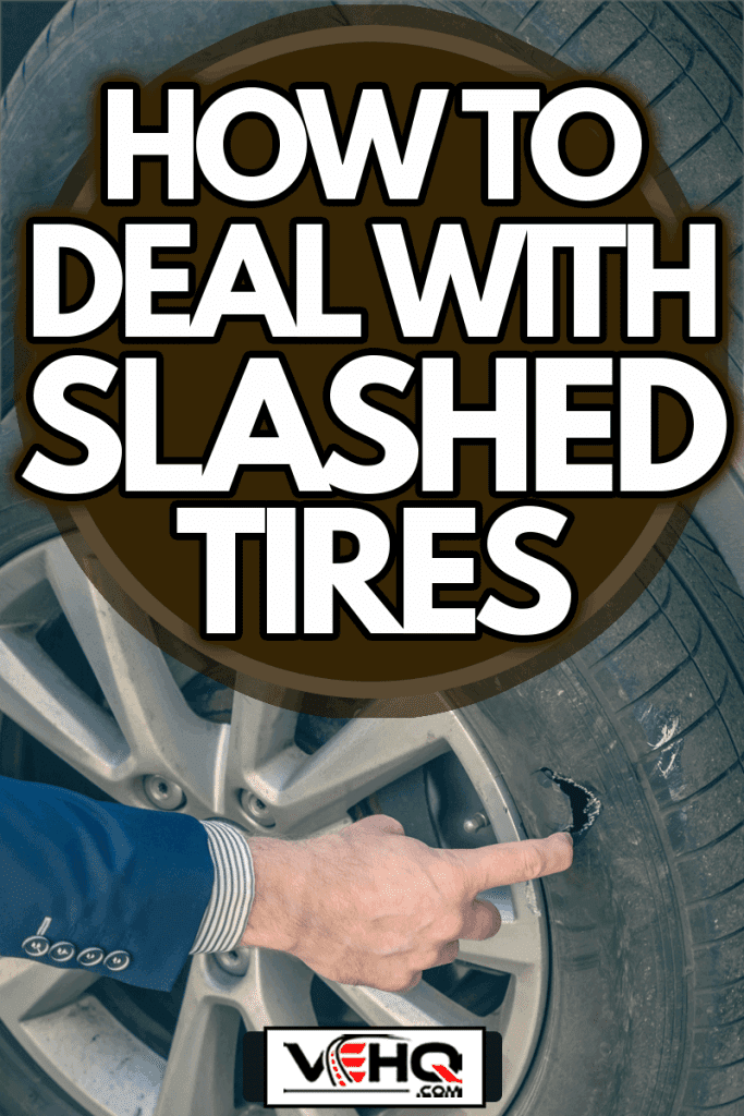 A businessman in a blue suit crouching near his car and checks the degree of damage to a punctured wheel, How To Deal With Slashed Tires