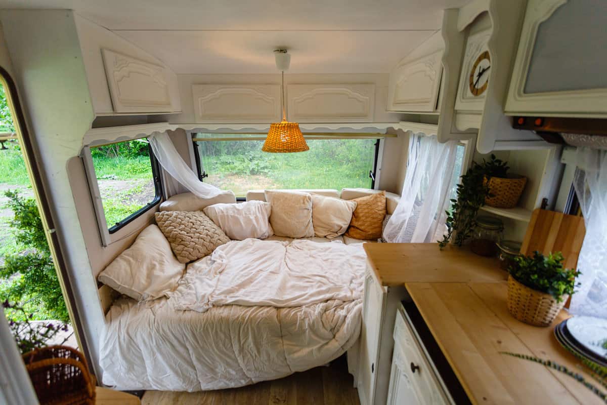 Inside the camper van. Unmade bed, pillows, white wooden interior decoration with lamp center. A cozy sleeping place for a young couple to sleep inside a camper for traveling.