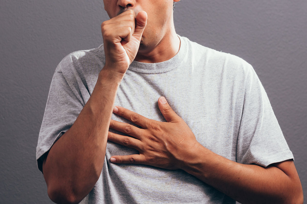 Man coughing into his fist, on a gray background