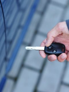 Man holding a keyfob near to blue car, How Close Does Key Fob Need To Be To Start Car?