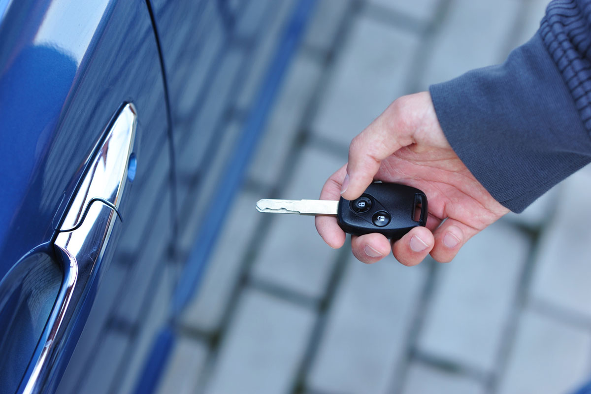 Man holding a keyfob near to blue car