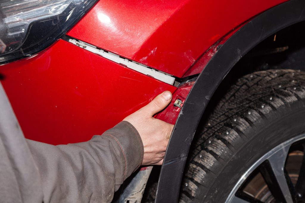 The hand of a man putting on or removing the front bumper from a red car in a vehicle repair shop. Industry in auto service.
