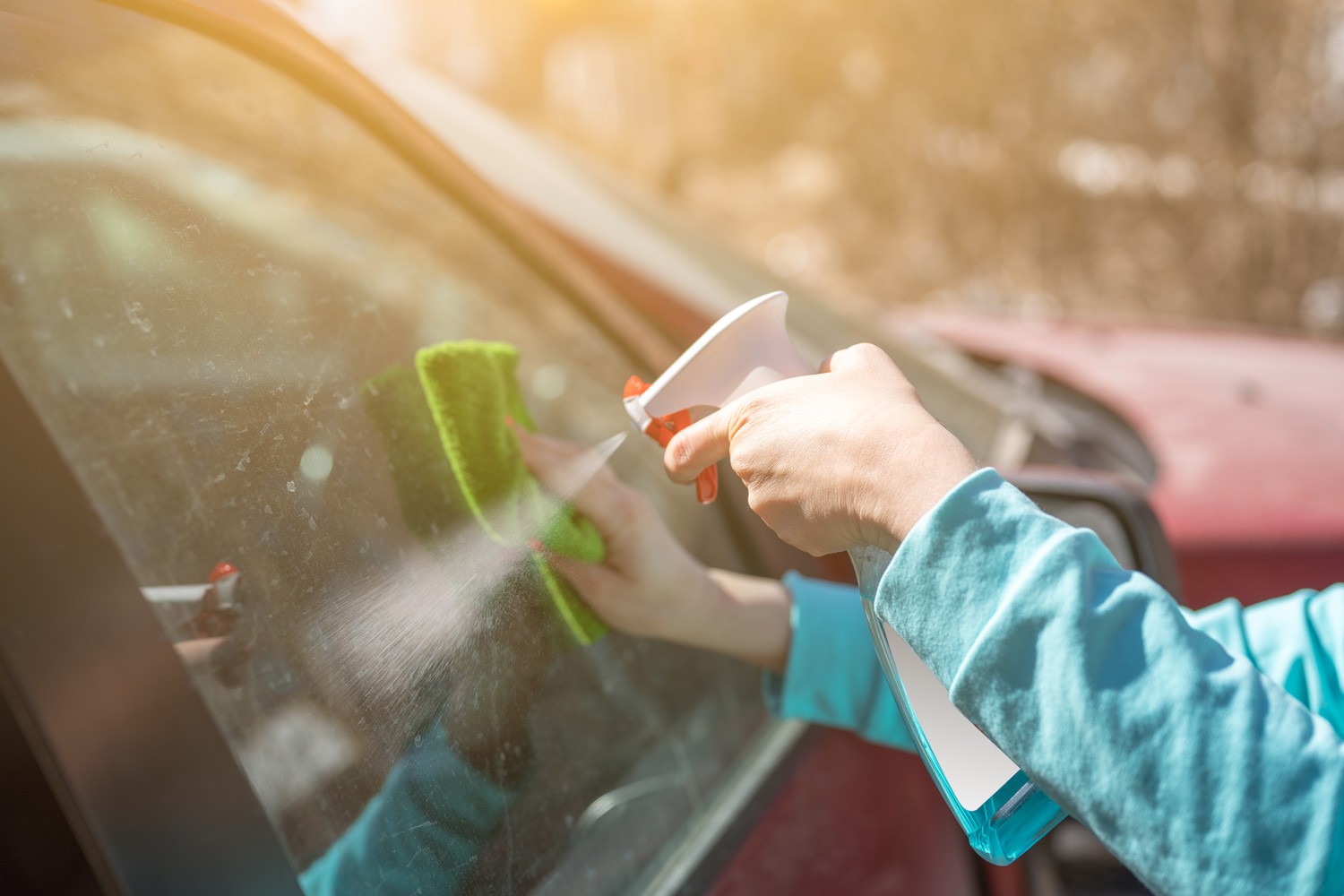 Woman Cleaning Car Windows with Spray Cleaner. female hand cleaning car window with microfiber cloth. Hand with Spray Cleaner wiping window of a car on a sunny day.