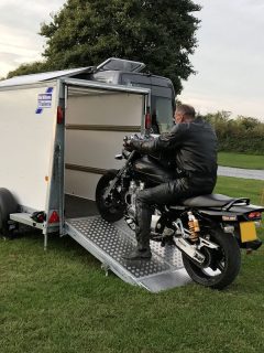 Yamaha XJR 1300 motorbike with motorcycle rider riding the bike into a secure covered trailer with red metal wheel lock on a campsite, How To Clean Toy Hauler Ramp Door