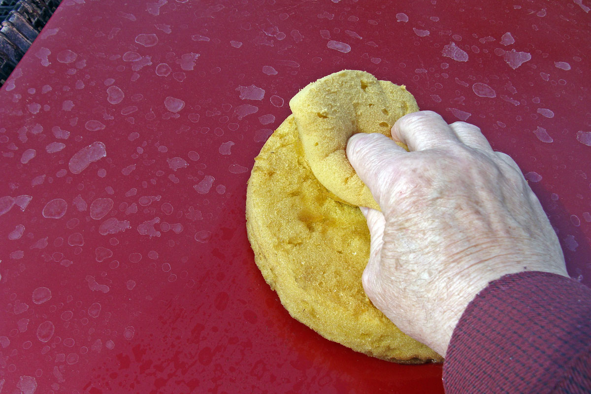 Yellow sponge and hand wearing white gloves while cleaning a red car