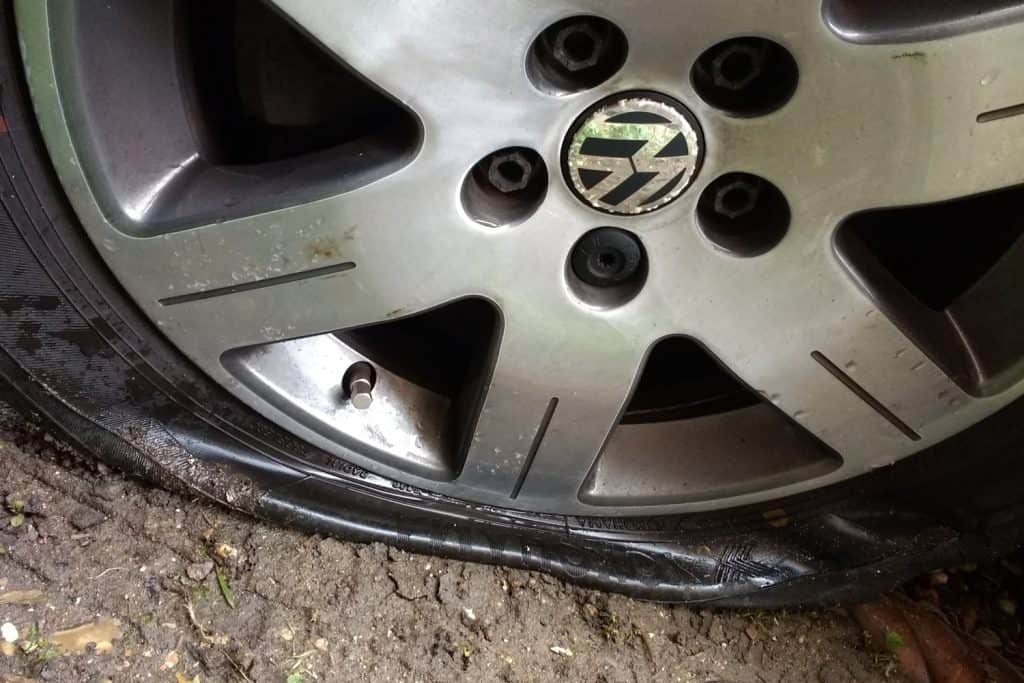 close up view of tyre puncture on VW Beetle car wheel showing black rubber flat after tear on road surface after accident