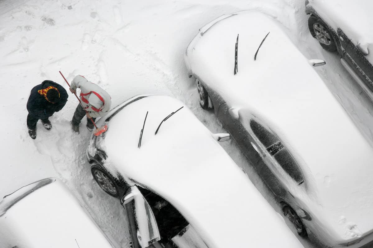 elevated view of two men cleaning snow covered car in parking lot.
