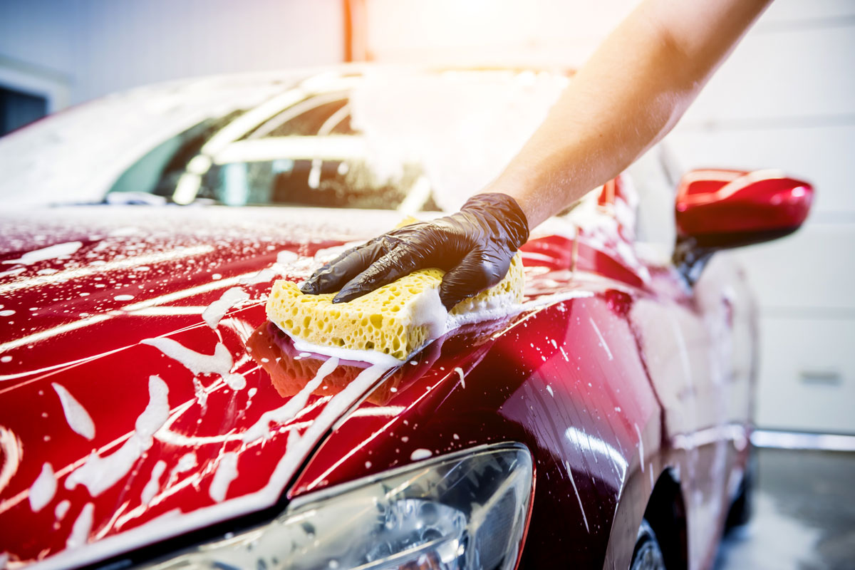 hand holding a yellow sponge while washing the red car