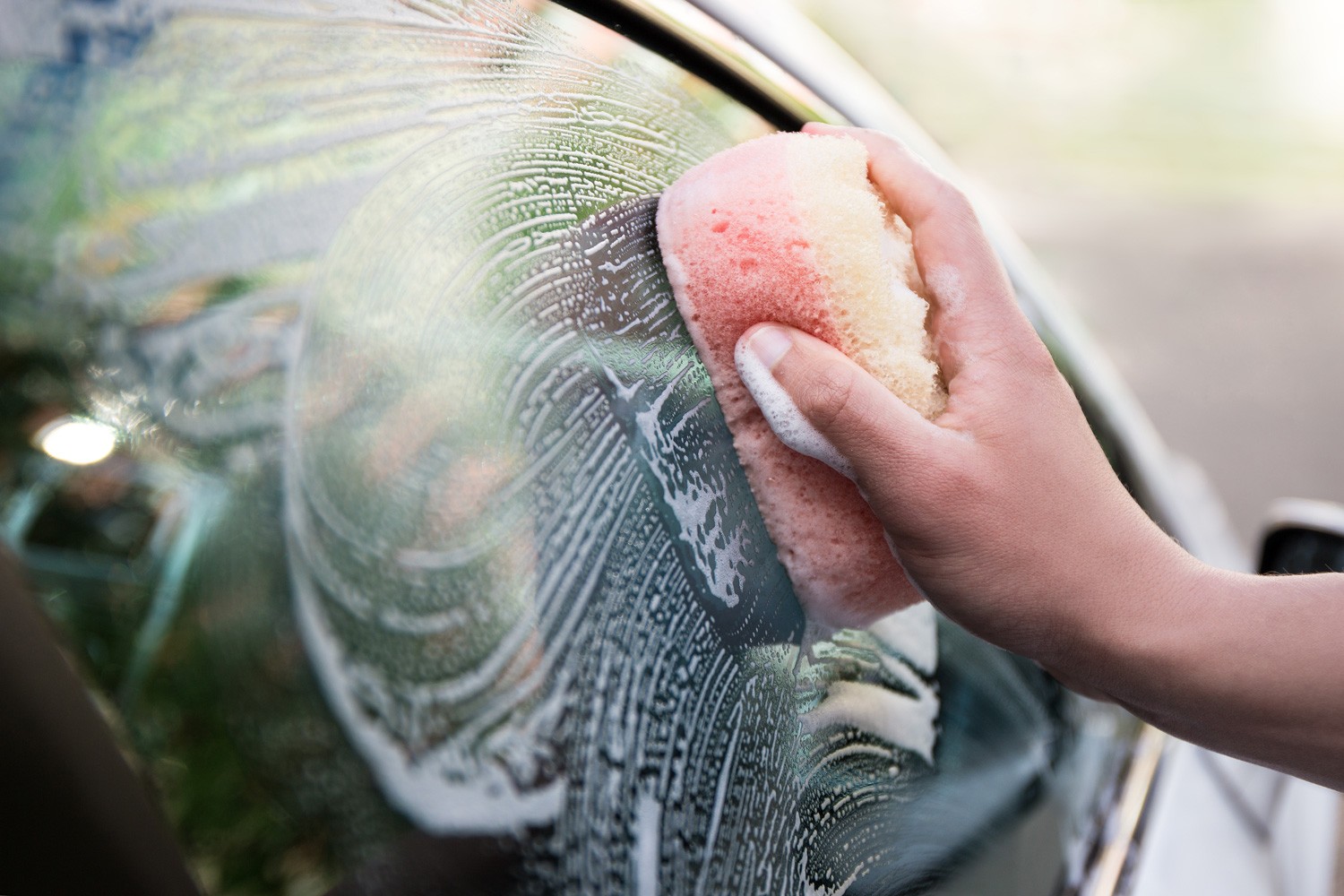 handle car wash concept - close up of male hand holding sponge and washing car window