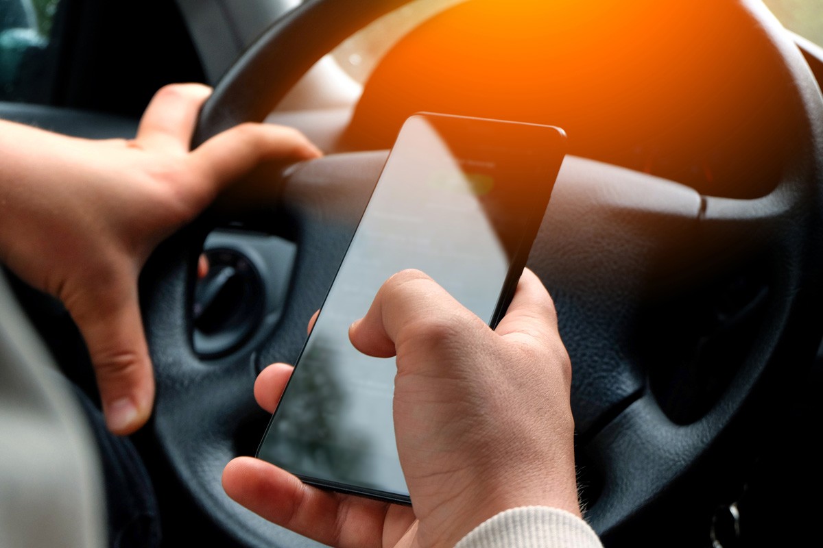 Safety concept: Car driver looks at smartphone while driving the car
