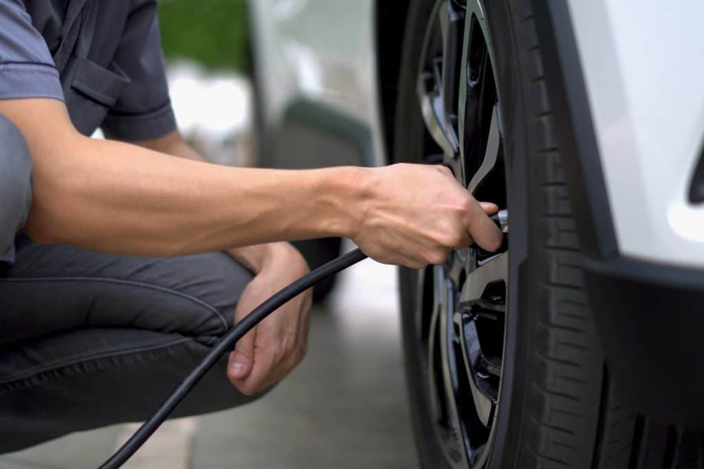 man filling air in the tires of his car (inflating tire)