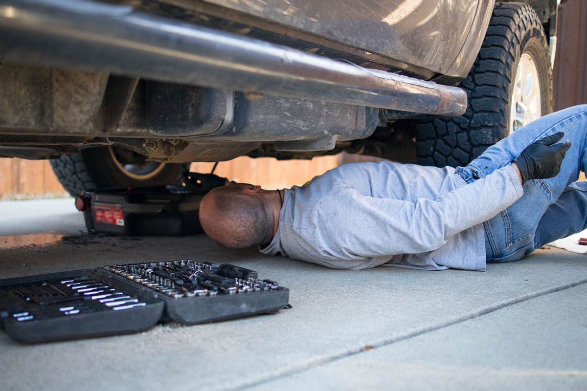 man lying under truck emptying the oil into an oil-pan while doing at-home DIY oil change