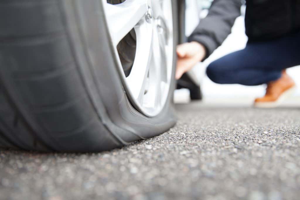 man touching a flat tire on the roadside