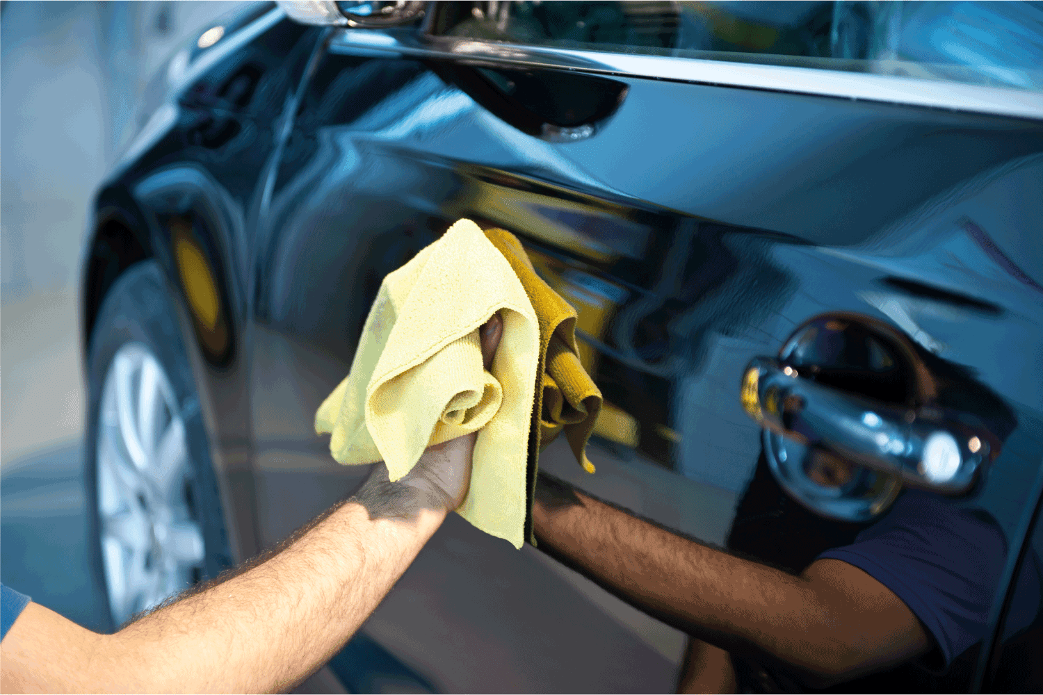 man wiping off excess water on car door using yellow cloth