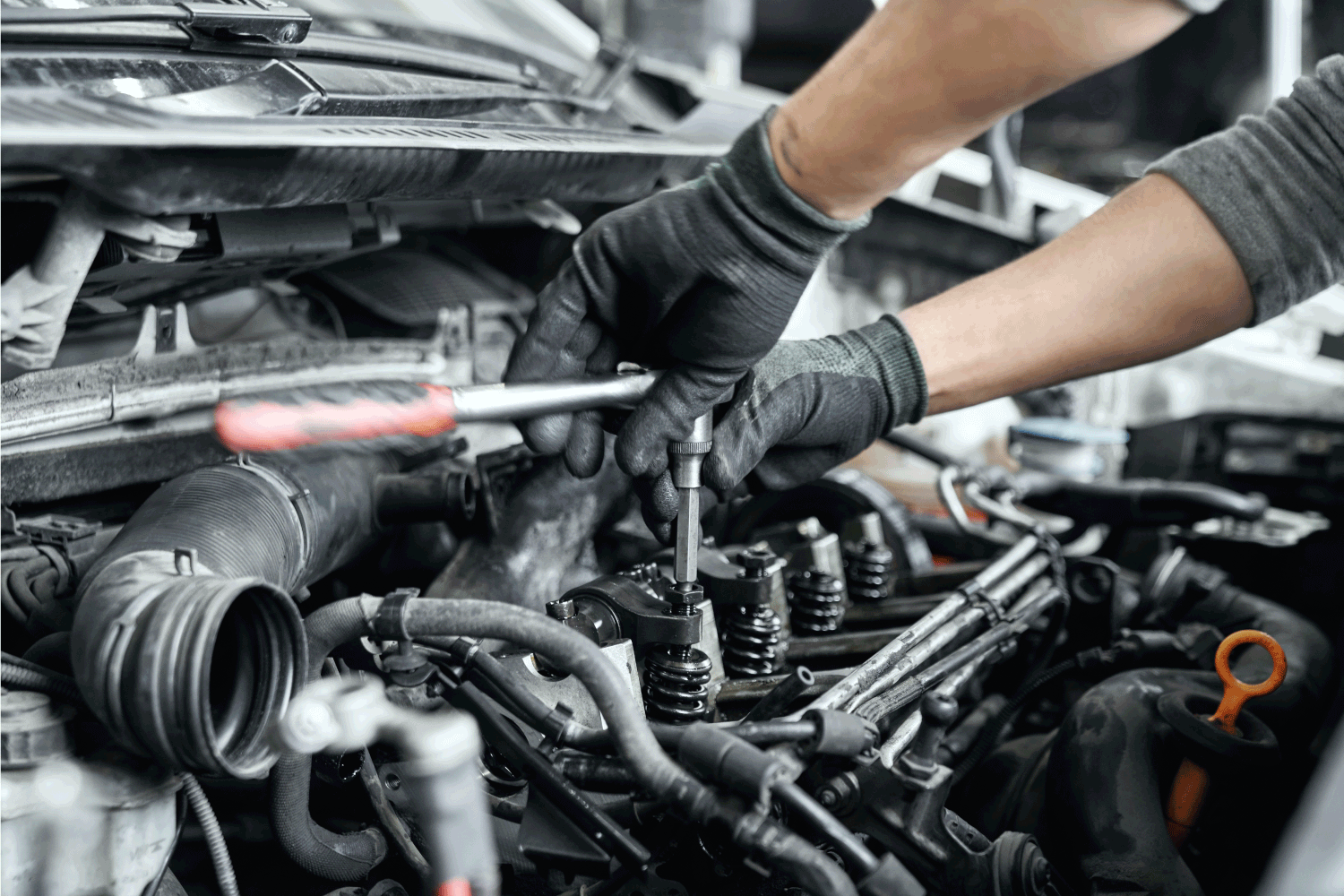 mechanic's hands in protective black gloves using wrench to remove spark plugs for repairing valve cover oil leaks