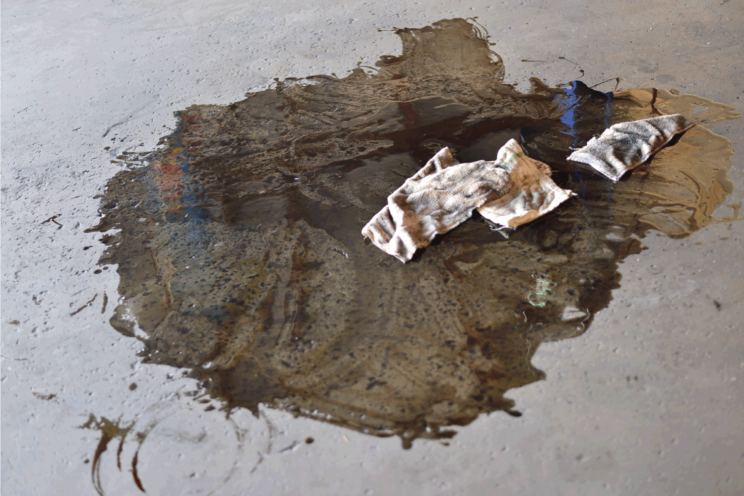 motor oil spill on auto shop floor leaving puddle of black motor oil with dirty soiled rags on the floor
