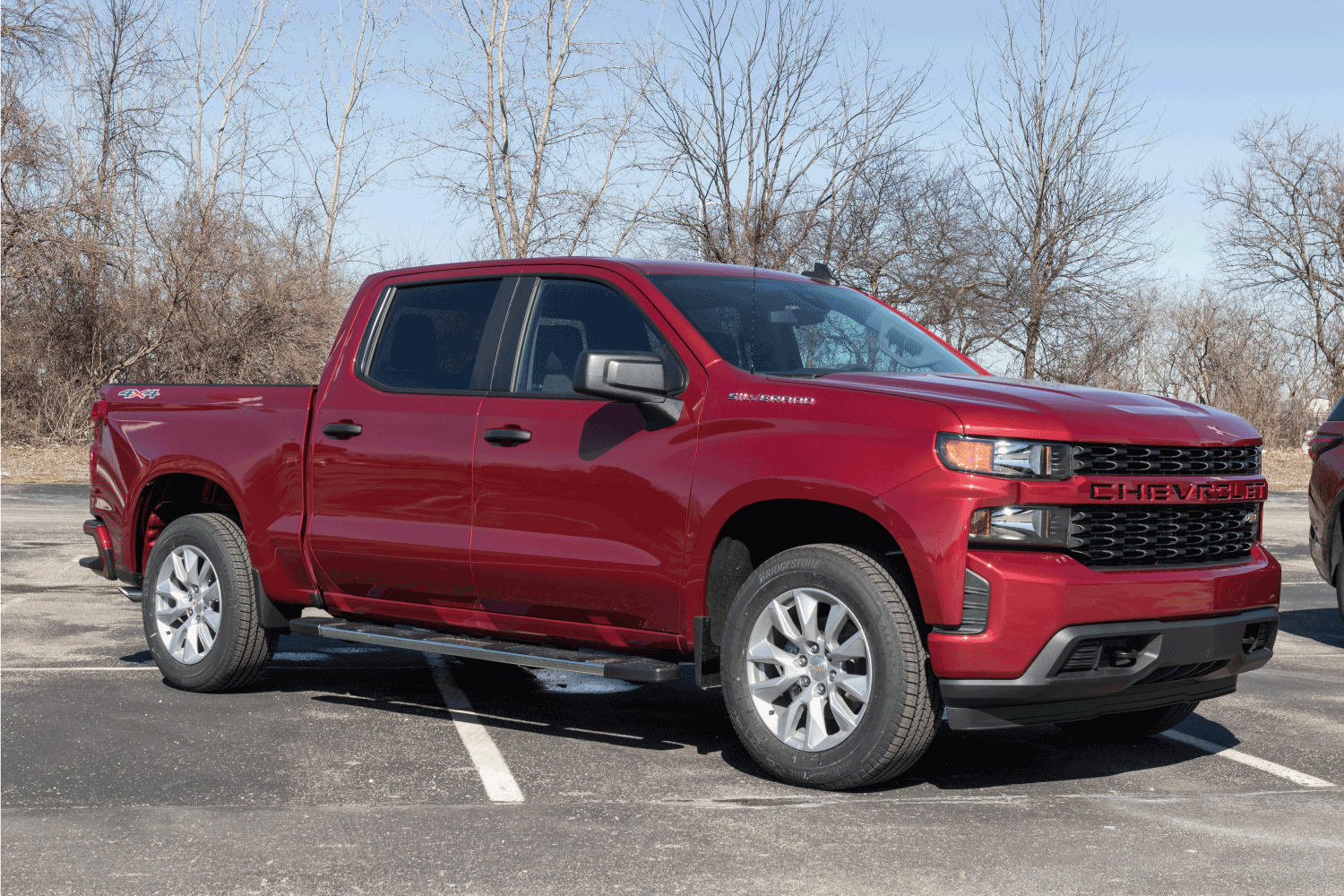 red chevrolet silverado parked on a open parking space with woods in the background