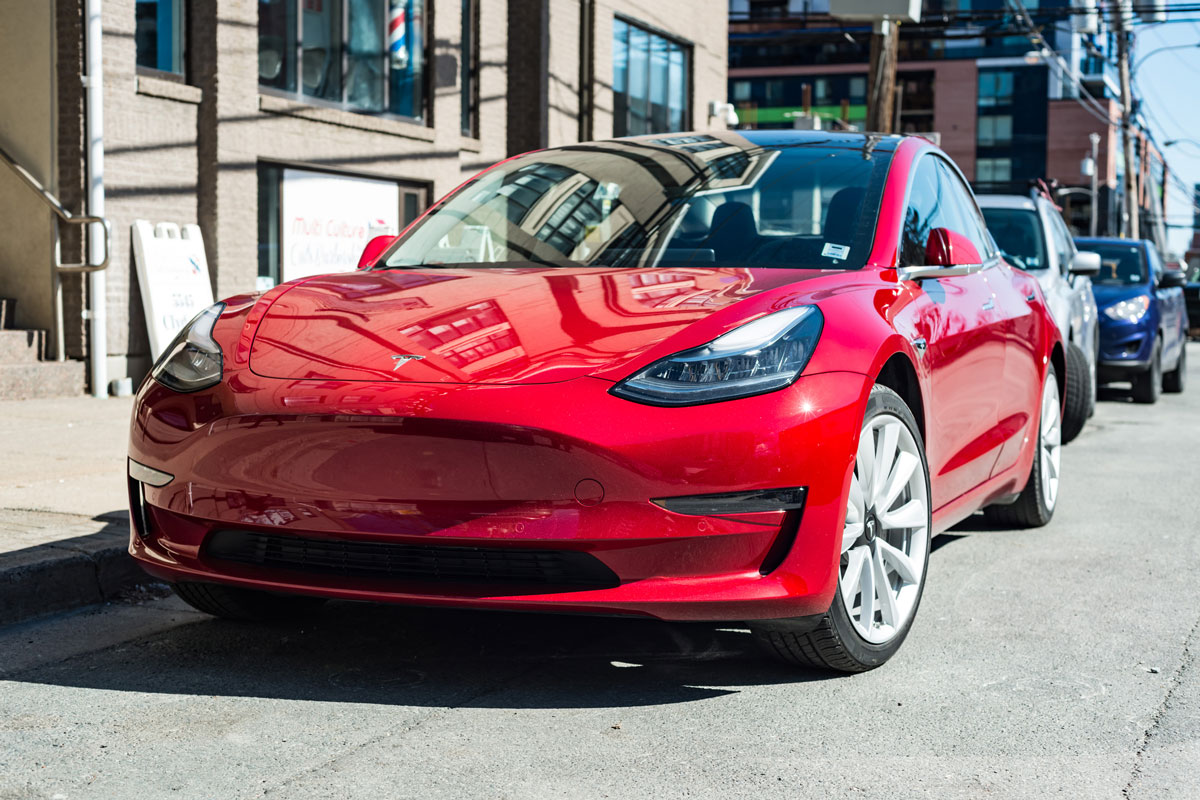 A 2019 red Tesla Model 3 plug-in electric car parked on a city street in downtown Halifax