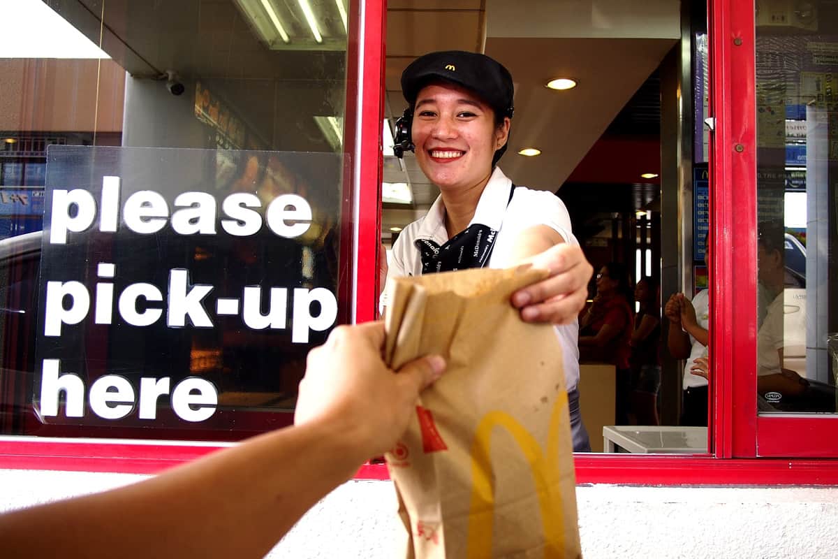 A service crew serves food to a customer at a drive thru counter.