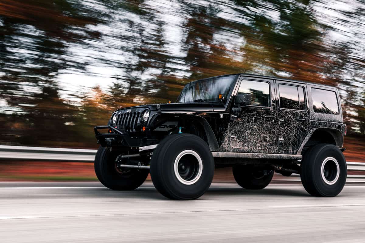 Black dirty Jeep Wrangler going fast on the road